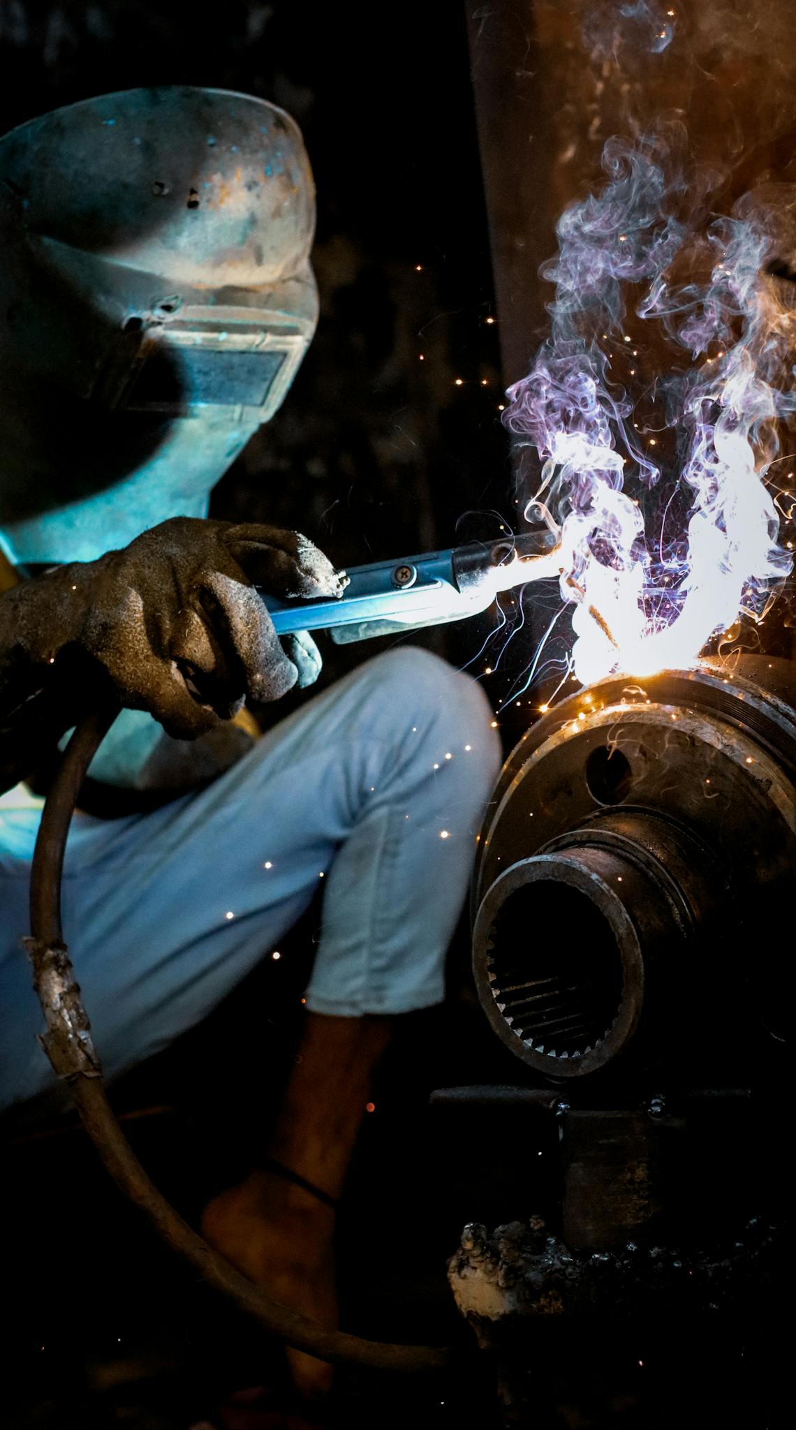 A welder working with sparks and smoke in an industrial setting in Dhaka, Bangladesh.